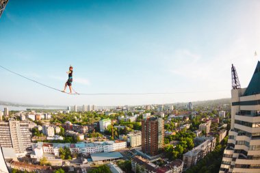 Bir adam bir hat boyunca yürüyor. Dört iki yüksek binalar arasında sıkı bir çizgi izler. Highline şehrin arka planı.