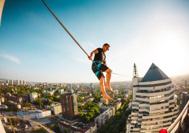 Bir adam iki bina arasında uzanan bir çizgi üzerinde oturuyor. Bir adam denge irtifada yakalar. Highline şehri.