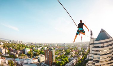 Bir adam iki bina arasında uzanan bir çizgi üzerinde oturuyor. Bir adam denge irtifada yakalar. Highline şehri.