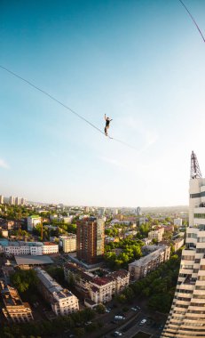Bir adam bir hat boyunca yürüyor. Dört iki yüksek binalar arasında sıkı bir çizgi izler. Highline şehrin arka planı.