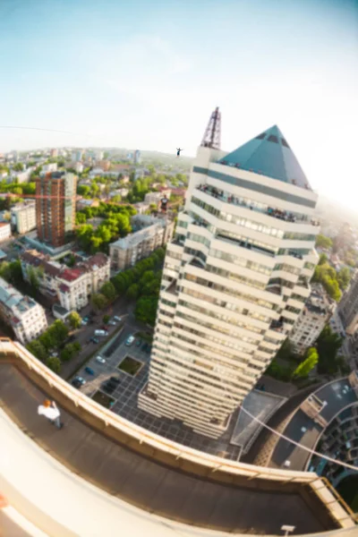 A man walks along a line stretched between two buildings. A man catches balance at altitude. Highline over the city.