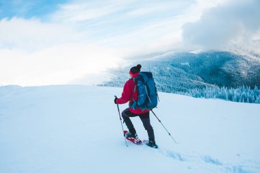Kar ayakkabılarını ve dağlarda trekking sopalarla bir adam. Kış gezi. Güzel bir gökyüzü bulutlu karşı bir dağcı, tırmanma. Aktif yaşam tarzı. Karda dağ tırmanma.