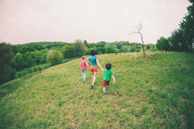 Çocuklu bir kadınla yeşil çim çalışır. Anne oğulları tarafından ellerini tutar ve çalıştırın. Açık havada ailesiyle birlikte oynayan bir çocuk. Çocuk annesi ve kardeşi ile çayırlarda yürür.