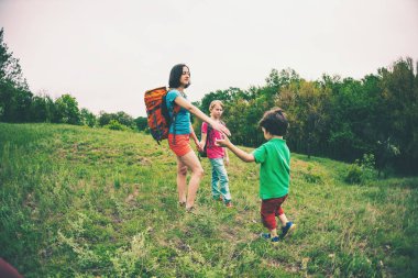 Çocuklu bir kadınla hiking gider. Aile ile seyahat. Çocuk ile kardeşi ve annesi Ormanda yürür. Sırt çantaları ile yürüyüş. Anne çocuk elini dışarı uzanır. Yardım eli.