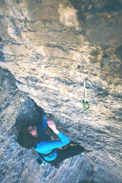 The girl climbs the rock. A woman overcomes a difficult climbing route. A rock climber on a rock. Doing sports outdoors.