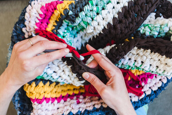 The woman is knitting crocheted out of thick yarn. Yarn from old clothes. Rug of homemade thread. Female hands hold the hook. Vintage carpet. Knitted plaid. Handmade. Home hobby.