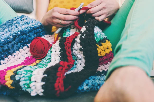 The woman is knitting crocheted out of thick yarn. Yarn from old clothes. Rug of homemade thread. Female hands hold the hook. Vintage carpet. Knitted plaid. Handmade. Home hobby.