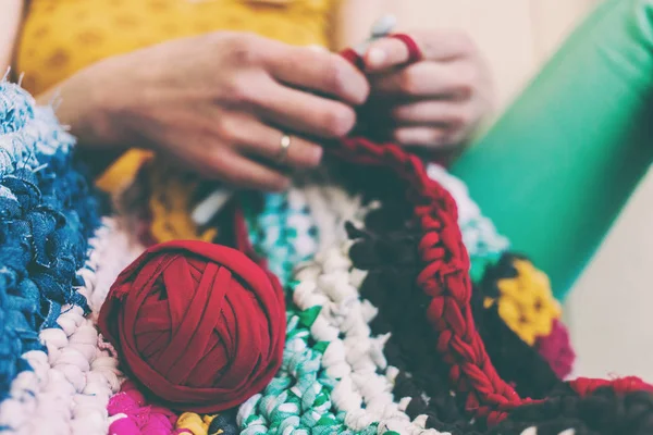 The woman is knitting crocheted out of thick yarn. Yarn from old clothes. Rug of homemade thread. Female hands hold the hook. Vintage carpet. Knitted plaid. Handmade. Home hobby.