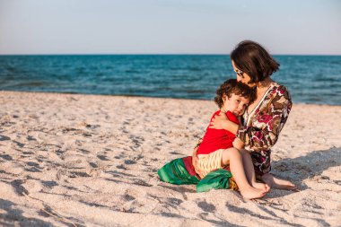Çocuk ile anne sahilde. Çocuk annesi ile oynuyor. Çocuk anne ve gülümsüyor sarılmak. Bir kadın oğluyla deniz kenarında dinleniyor.