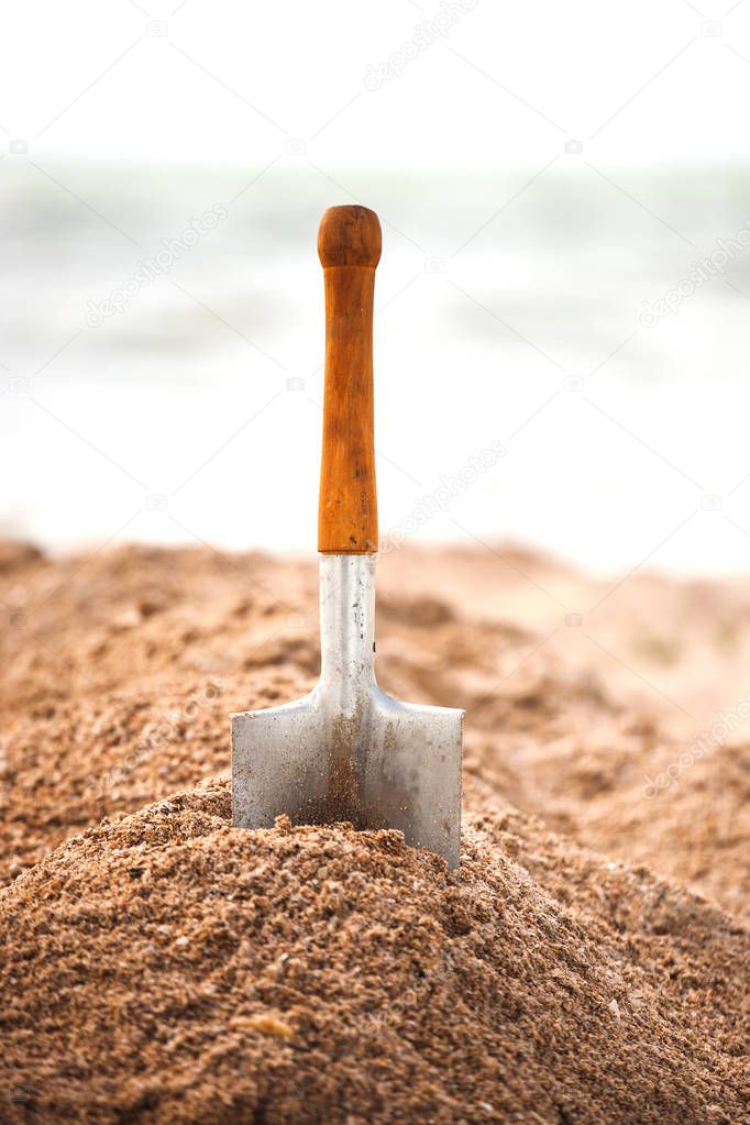 A metal spade in the sand. Children's shovel on the seashore. Working tool against the background of the sea coast.