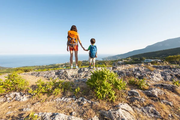 女性は子供と一緒に旅行している 山の中の母と息子 子供と一緒に山の頂上に登る リュックを背負った少年は上に登った 休暇中 — ストック写真