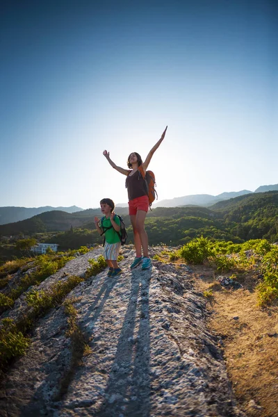 A woman is traveling with a child. Mother and son in the mountains. Climb to the top of the mountain with children. The kid with the backpack climbed to the top. The girl raised her hands up.