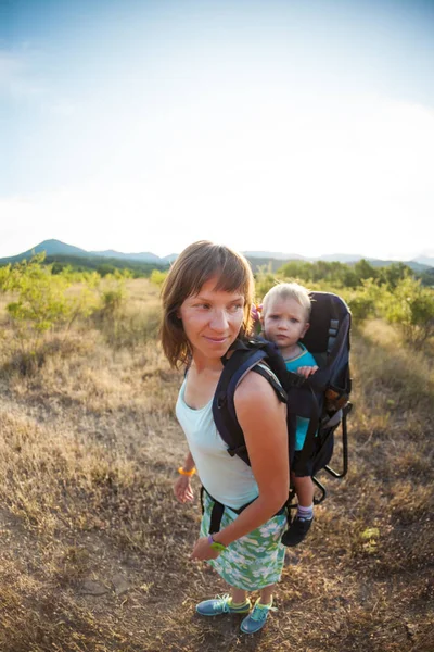 Bir oğlan bir sırt çantası içinde oturuyor. Çocuk ailesiyle birlikte dolaşıyor. Bir çocukla tırmanma. Anne Bebek taşır. Küçük bir seyahat. Bir kadın bebeği ile bir sırt çantası taşıyor.