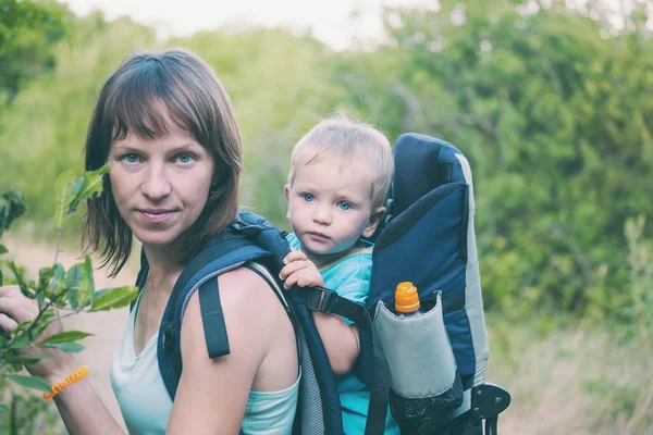 Bir oğlan bir sırt çantası içinde oturuyor. Çocuk ailesiyle birlikte dolaşıyor. Bir çocukla tırmanma. Anne Bebek taşır. Küçük bir seyahat. Bir kadın bebeğini taşıyor. Çocuklarla seyahat.