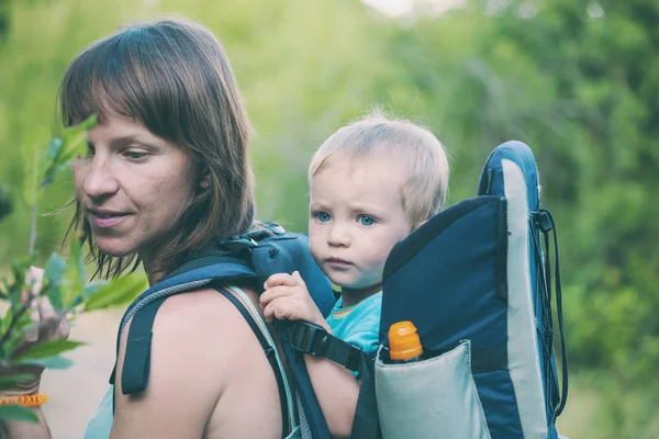 Bir oğlan bir sırt çantası içinde oturuyor. Çocuk ailesiyle birlikte dolaşıyor. Bir çocukla tırmanma. Anne Bebek taşır. Küçük bir seyahat. Bir kadın bebeğini taşıyor. Çocuklarla seyahat.