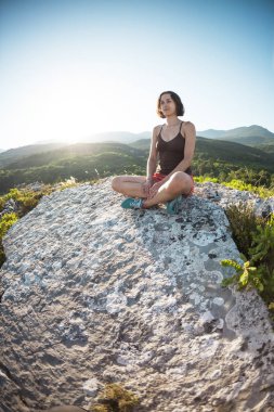 Bir kız günbatımında bir dağın tepesinde oturuyor. Bir kadın yoga devreye girer. Meditasyon medeniyet çok uzak olduğunu. Güzel doğa ve tefekkür. Dağları nın görünümü.