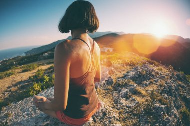 Bir kız günbatımında bir dağın tepesinde oturuyor. Bir kadın yoga devreye girer. Meditasyon medeniyet çok uzak olduğunu. Güzel doğa ve tefekkür. Dağlar ve deniz görünümü.