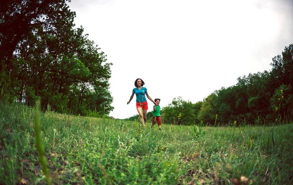 Bir kadın ve oğlu yeşil çim çalışıyor. Anne Çocuk gülüyor ve el tarafından tutar. Bir çocuk annesi doğa ile oynuyor. Çocuk çayırlarda yürür.