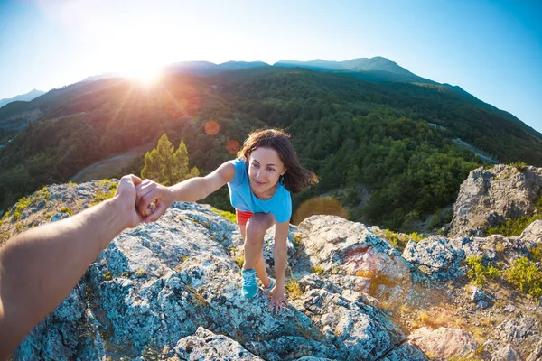 A woman is climbing a stone. Helping hand. A friend helps a girl to climb a mountain. Teamwork. Climbing at sunset.