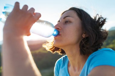 İçme suyu bir dağın tepesinde bir kadındır. Kız onun susuzluk quenches. Yorgun turistik bir plastik şişeden içer. Esmer su ağzının kenarında bir şişe tutuyor.