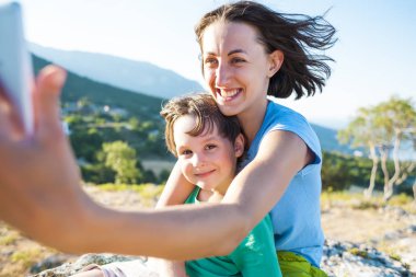 Bir kadın bir dağın tepesinde bir çocukla. Anne ve oğlu selfie güzel bir manzara arka plan üzerinde olun. Bir çocukla seyahat.