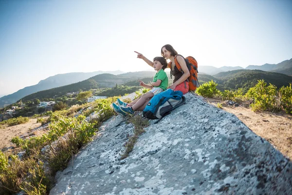 A woman is traveling with a child. Mother with a son is sitting on a large rock. Climb to the top of the mountain with children. The boy with the backpack climbed to the top. Active vacations.