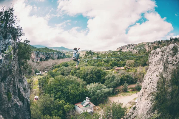 A woman catches balance on the line. Performance athlete in the passage of the sling at high altitude. Exercise in nature. Danger and insurance. The girl is sitting on the line. Trying to get up.