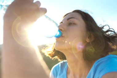 İçme suyu bir dağın tepesinde bir kadındır. Kız onun susuzluk quenches. Yorgun turistik bir plastik şişeden içer. Esmer su ağzının kenarında bir şişe tutuyor.