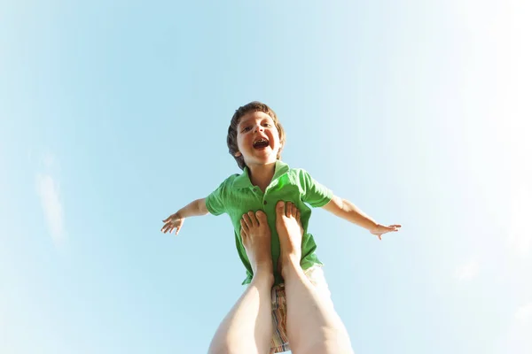 少年は母の足で飛行機のように飛ぶ 青空子 子供とお母さんは 自然にヨガに取り組んでいます 女性は彼女の息子を楽しませる — ストック写真