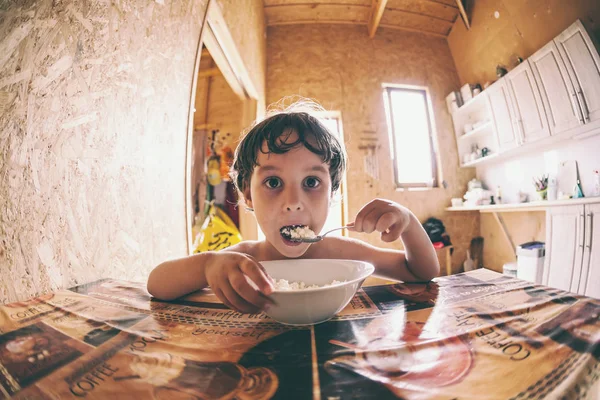 the boy eats a cottage cheese spoon sitting at a table in a spacious dining room.