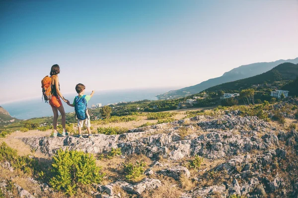 A woman is traveling with a child. Mom and son in the mountains. Climb to the top of the mountain with children. The boy with the backpack climbed to the top. Active vacations.