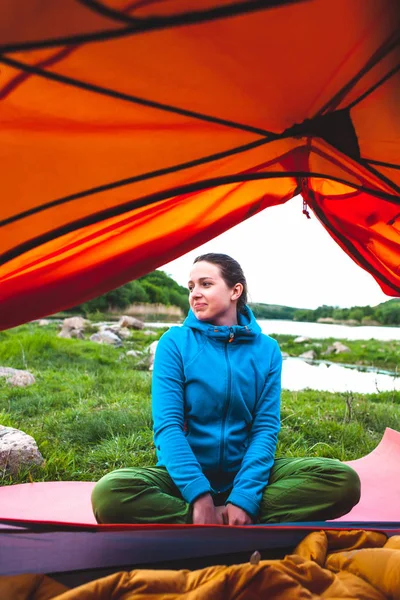 女の子はテントの近くに座っています スリーピング バッグの女性 笑顔ブルネットは 本質的に休んでいます 川でキャンプ — ストック写真