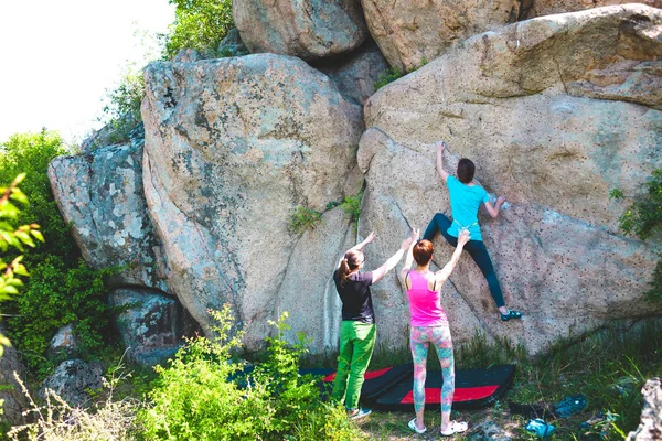在自然里爬山 朋友爬到那块石头 这个女孩爬上石头 和朋友支持她 在自然的抱石 积极的生活方式 运动的人 体操保险 — 图库照片