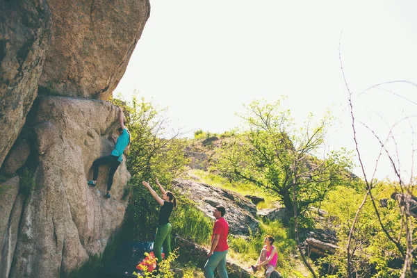 在自然里爬山 朋友爬到那块石头 这个女孩爬上石头 和朋友支持她 在自然的抱石 积极的生活方式 运动的人 体操保险 — 图库照片