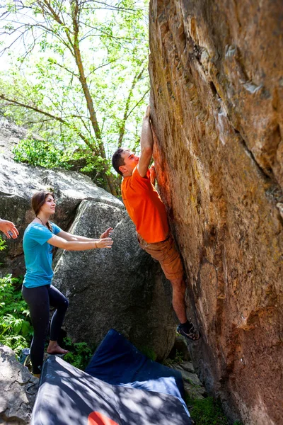 一个攀岩者爬上一块石头 他的搭档保险 运动员在户外抱石赛 一群在新鲜空气中参与体育运动的朋友 男人和女人在大自然中休息 — 图库照片
