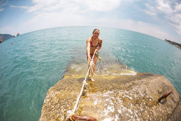 穿着泳装的女孩站在防波堤上 一个女人站在码头上 金发女郎从水里出来了 在海上休息 一名女运动员正在练习从码头上跳下去 鱼眼镜片 — 图库照片