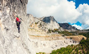 Bir kayaya dağcı. Kız güzel dağ manzarası ve bulutlu gökyüzü arka plan üzerine kaya tırmanıyor. Aktif yaşam tarzı. Doğa sporları. Zor bir tırmanış rota üstesinden gelmek.