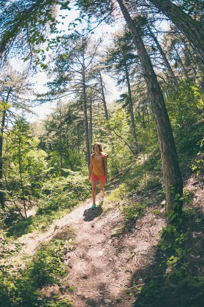 The girl is walking through the forest. A young woman with a backpack travels through picturesque places. A tourist walks along a mountain path. Fisheye lens.