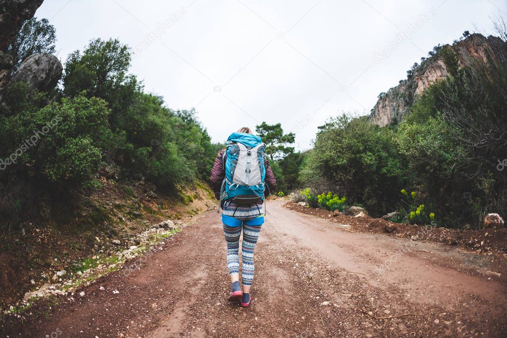 The climber is preparing for the ascent. A woman in a safety system and with a backpack approaches the climbing route. Mountain climbing. Fitness in nature. Mountaineer is walking along a stony path.