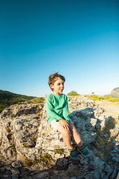 山の上に少年 児バックパック旅行です 山と美しい空の背景の子供します アクティブな休暇 ほとんどの旅行者は石に座っていません — ストック写真