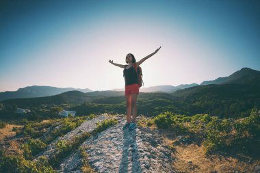 Dağın zirvesine kıza. Bir kadın bir sırt çantası ile bir kayada duran ve elleri kadar yükselterek. Yukarı tırman. Güzel yerlere seyahat. Turist gökyüzüne karşı.