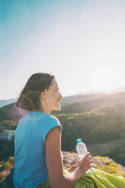 İçme suyu bir dağın tepesinde bir kadındır. Yorgun turistik bir plastik şişeden içer. Esmer günbatımında bir uyku tulumu içinde oturuyor. Kız onun elinde bir şişe su tutuyor.