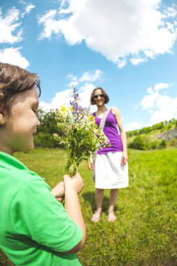 Çocuk annesi bir buket çiçegi verir. Bir kadın bir çayırda oğluyla yürüyor. Anneler günü için bir hediye. Kız çiçek bir grup alır. Çocuk Anne kutladı.