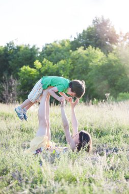Anne oğlu aktif oyunlar oynuyor. Jimnastik alanında bir çocukla. Çocuk Anne bacaklarına yalan söylüyor. Kadın bebek ayağa yükseltir. Çimenlerin üzerinde bir çift yoga. Akroyoga.