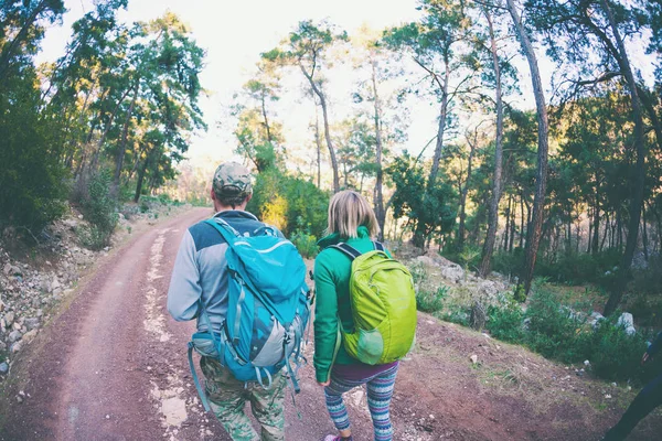 Friends go on a stony road. A woman and a man are walking in the park. A couple with backpacks travels to beautiful places. Tourists go along the mountain road.