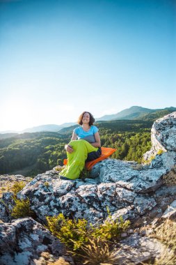 Bir kadın bir dağın tepesinde bir uyku tulumu içinde oturuyor. Gülümseyen bir kız bir tırmanış sonra aittir. Esmer dağlar ve batan güneşin arka plan kendini şişirme mindere oturur.
