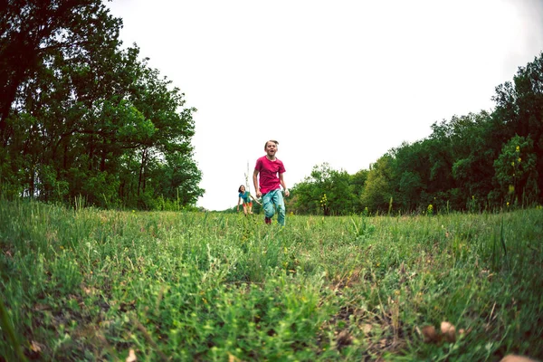 一个带着孩子的女人沿着绿草奔跑 妈妈赶上了儿子 一个男孩和他的家人在户外玩耍 那孩子和他的朋友们在草地上散步 — 图库照片