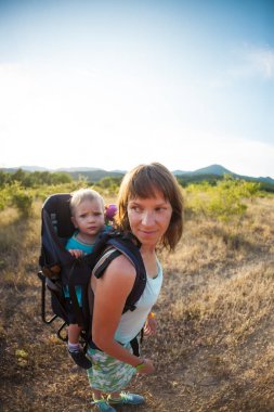 Bir oğlan bir sırt çantası içinde oturuyor. Çocuk ailesiyle birlikte dolaşıyor. Bir çocukla tırmanma. Anne Bebek taşır. Küçük bir seyahat. Bir kadın bebeği ile bir sırt çantası taşıyor.