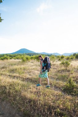 Bir oğlan bir sırt çantası içinde oturuyor. Çocuk ailesiyle birlikte dolaşıyor. Bir çocukla tırmanma. Anne Bebek taşır. Küçük bir seyahat. Bir kadın bebeğini taşıyor. Çocuklarla seyahat.