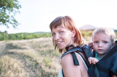 Bir oğlan bir sırt çantası içinde oturuyor. Çocuk ailesiyle birlikte dolaşıyor. Bir çocukla tırmanma. Anne Bebek taşır. Küçük bir seyahat. Bir kadın bebeği ile bir sırt çantası taşıyor.